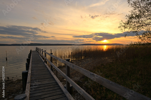 Abendrot an einem See, in den ein Bootssteg aus Holz führt.