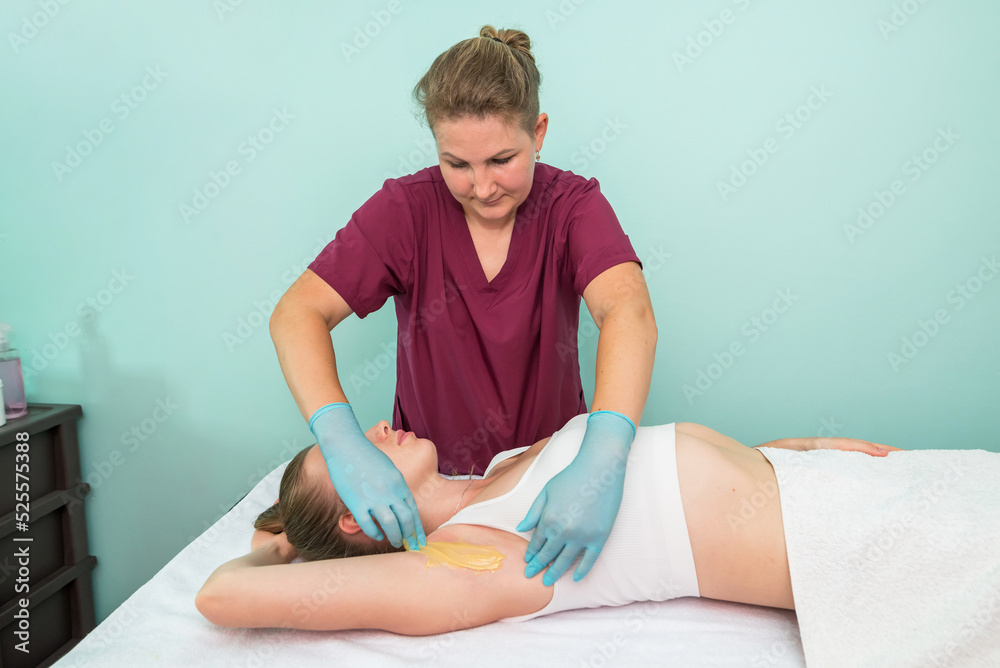 Depilation and epilation of the female armpit with liquid sugar paste. The beautician's hand applies wax paste to the armpit. Depilation and epilation of the female armpit with liquid sugar paste. The beautician's hand applies wax paste to the armpit.