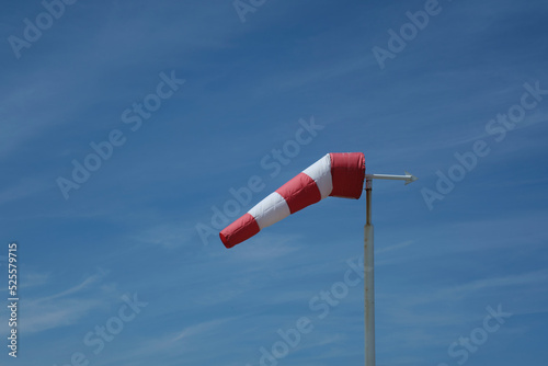 Red-white windsock against the blue sky in sunny weather. Wind vane indicates the strength and direction of the wind