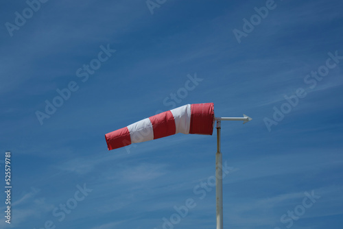 Red-white windsock against the blue sky in sunny weather. Wind vane indicates the strength and direction of the wind