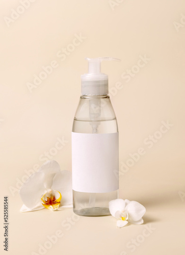 Cosmetic pump dispenser bottle near white orchid flowers on light beige close up. Mockup