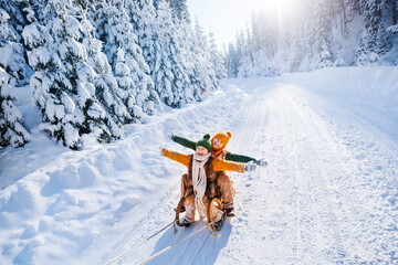 Happy funny children ride wooden retro sleds on snowy road in mountains. Family on winter walk.