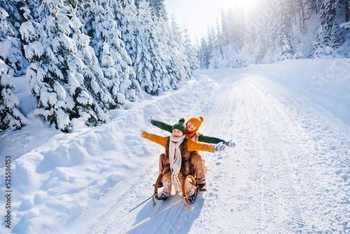 Happy funny children ride wooden retro sleds on snowy road in mountains. Family on winter walk.