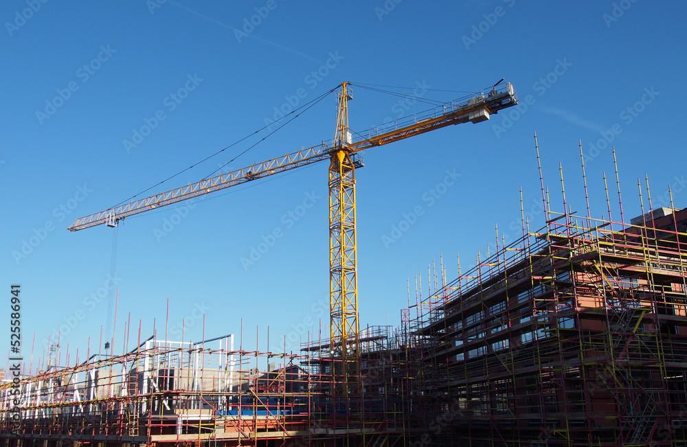 yellow construction crane working on a large modern apartment development with scaffolding with blue sky and sunlight
