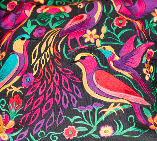 Handmade colorful fabric from Chiapas, Mexico. Birds and flowers edged in various colors on a black background.