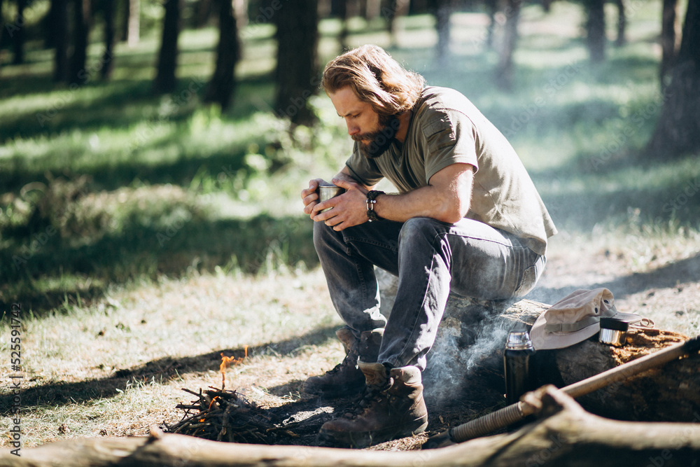 Man sits by fire in forest and drinks hot tea Man sits by fire in forest and drinks hot tea