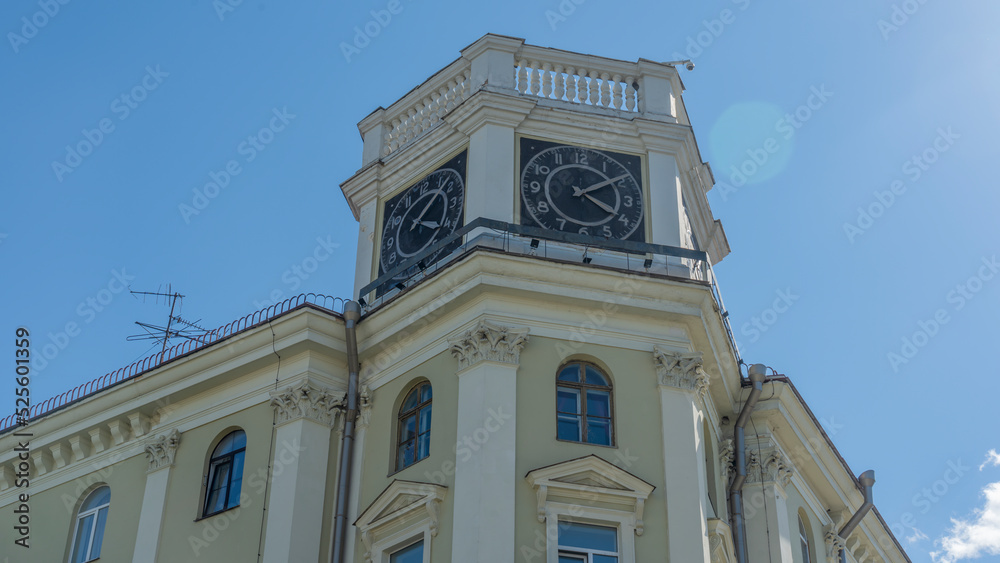 The vintage clock tower on facade of the residential building on blue sky background with sun glare. Urban backgrouund.
