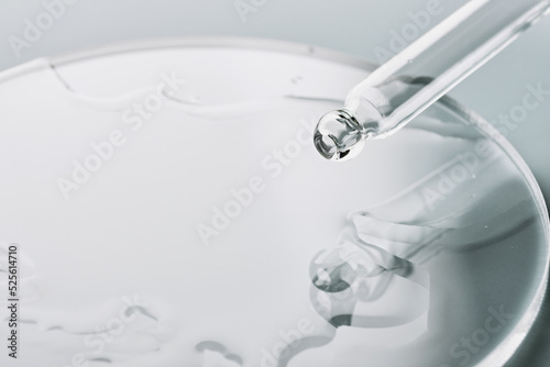 Pipette with sample of cosmetic product in petri dish on grey background, selective focus