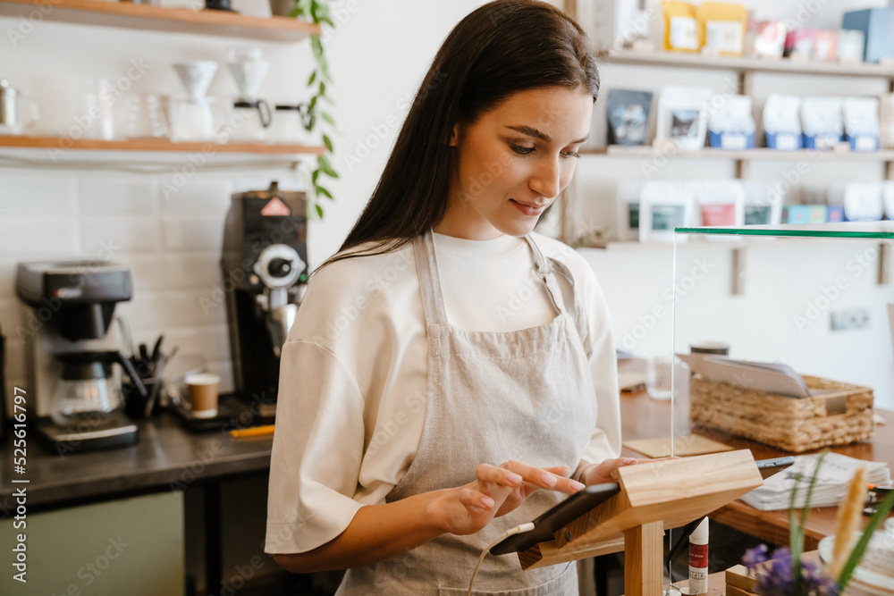 White barista woman wearing apron working with tablet computer in cafe White barista woman wearing apron working with tablet computer in cafe