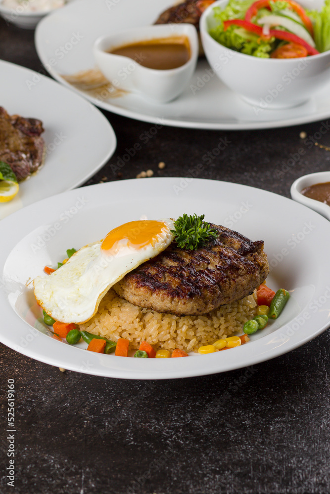 Grilled beef steaks with potato, vegie and steak sauce at white plate on texture rustic table