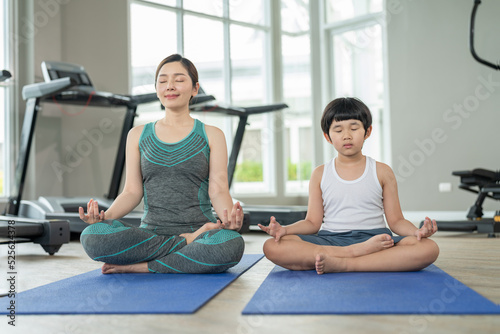Happy Asian mother and son wearing sportswear practices yoga together in small gym sports club