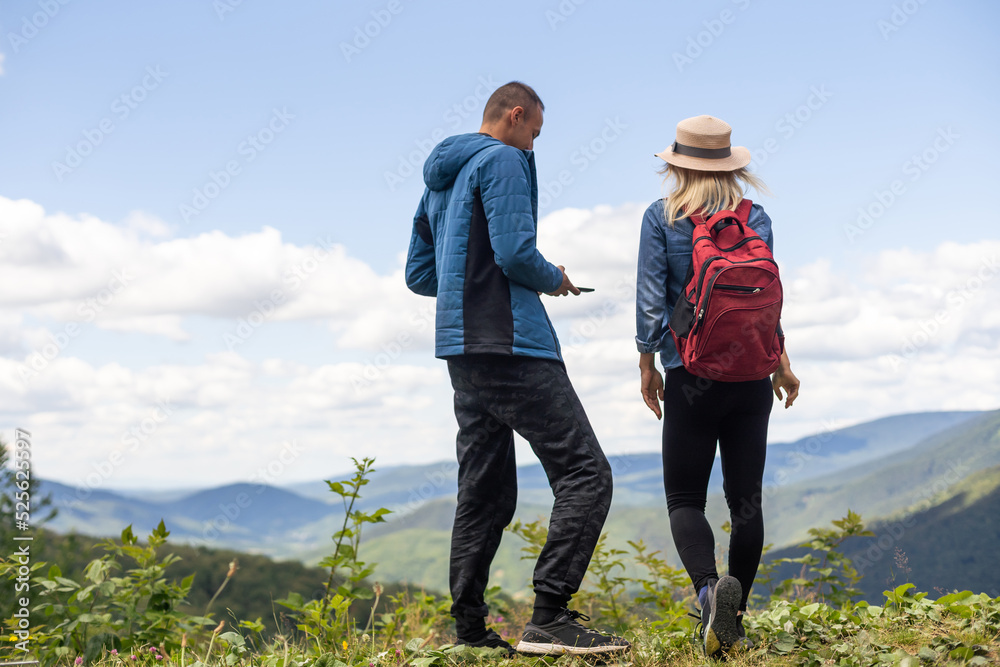 Rear view of hiking couple with backpack standing together on hill top enjoying beautiful landscape. Man and woman outdoors on hiking standing on a rock