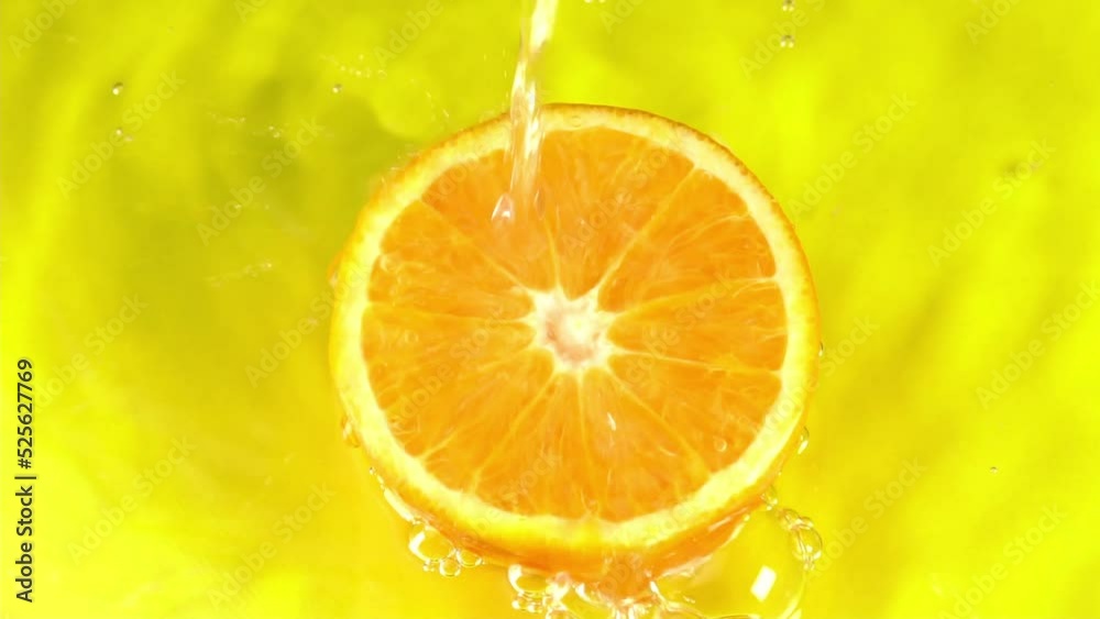 Water pours on an orange juicy orange on a yellow background slow motion closeup. Orange slice and water splashing and juicy fruit background. Making cocktail of fruits, drinking cold lemonade Water pours on an orange juicy orange on a yellow background slow motion closeup. Orange slice and water splashing and juicy fruit background. Making cocktail of fruits, drinking cold lemonade