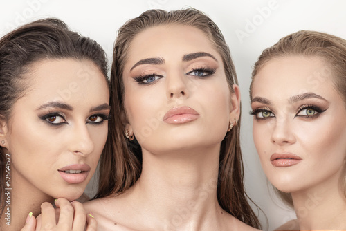 Studio portrait of three beautiful and sexy women with smoky make-up and wet hair standing near each other and looking to camera with seductive look. Models with green, brown and blue eyes