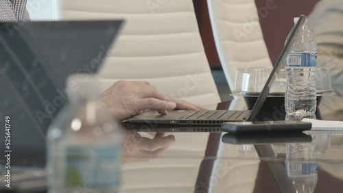Film Pan of Hands Typing on Laptops on Glass Table in Business Meeting With Water Bottles and Food Takeout Containers