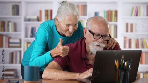 Portrait of senior man and woman at home working on laptop computer doing taxes and get good report. Concept of success couple working together.