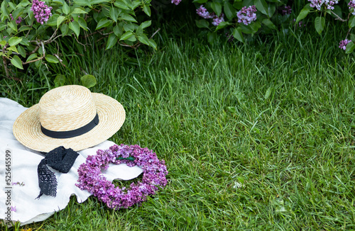 a wreath of lilacs and hat on a white plaid in the park