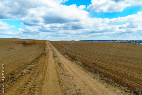 A dry sandy road passes through a field under the scorching sun and clouds. Dirt road outside the city in the village. Arid climate on earth. Climate change and its consequences.