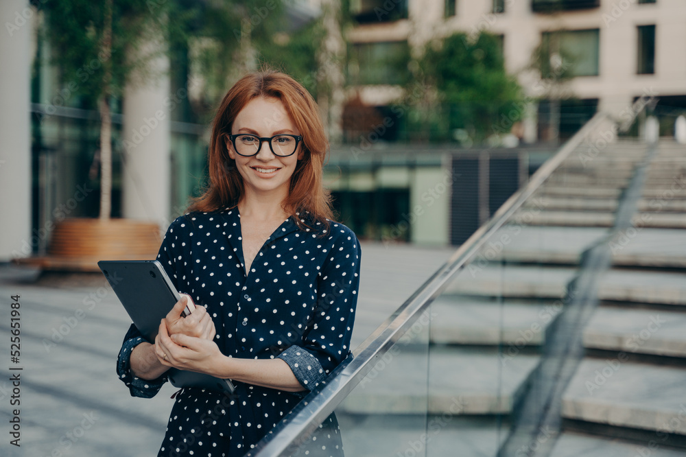 Positive redhead young woman in stylish outfit carries notepad poses outdoor Positive redhead young woman in stylish outfit carries notepad poses outdoor