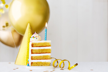 Slice of birthday cake with blue birthday candle and gold balloons