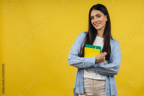 Portrait of cheerful young woman student in classic clothes, with backpack holding books isolated on yellow background. Education in high school university college concept