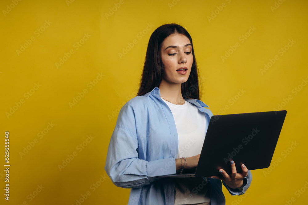 Portrait of a happy young brunette girl using laptop computer isolated over yellow background Portrait of a happy young brunette girl using laptop computer isolated over yellow background