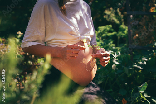 It's triplets! Pregnant woman in the garden with triplets in her belly, holding three sprouted plants