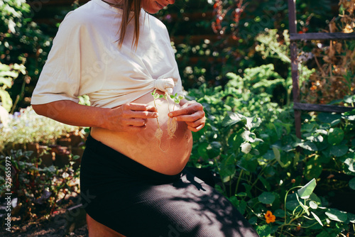 It's triplets! Pregnant woman in the garden with triplets in her belly, holding three sprouted plants