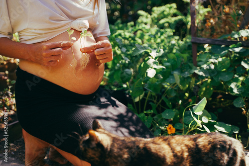It's triplets! Pregnant woman in the garden with triplets in her belly, holding three sprouted plants