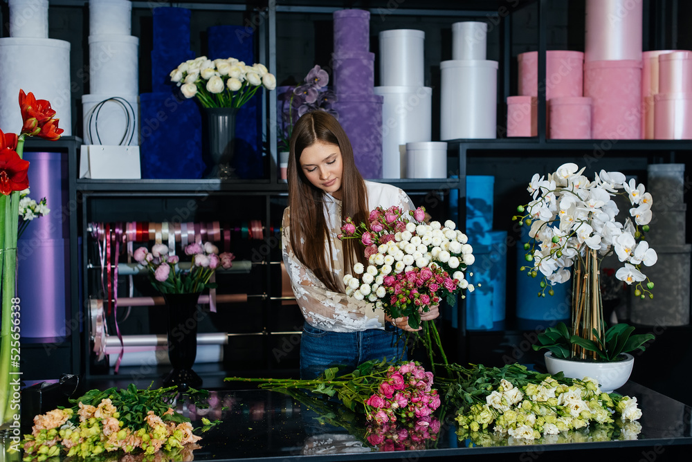 A young female florist takes care of flowers in a cozy flower shop and collects bouquets. Floristry and making of buckets in a flower shop. Small business.