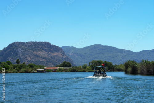 Tourist pleasure boat on Dalyan River, next to rocks, which contain Lycian tombs, in Mugla Province located between districts of Marmaris and Fethiye on south-west coast of Turkey