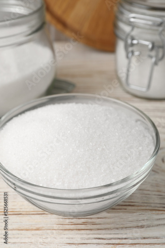 Granulated sugar in glass bowl on white wooden table, closeup