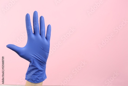 Person in medical gloves on pink background, closeup of hand. Space for text