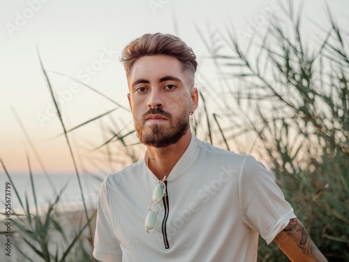 Portrait of a Caucasian guy with a beard and piercing, looking into the camera at sunset