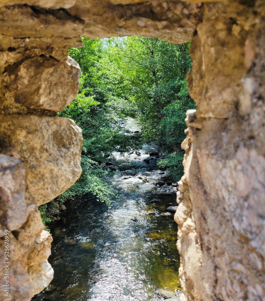 Beautiful view of the river between the stones located in Villefranche del Conflent, France. View through a hole in the wall. Natural landscape. River background with space for text.