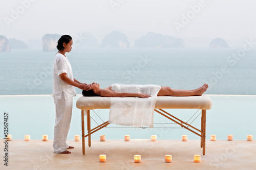 A woman receives a candlelit poolside massage at dusk at a  three-bedroom private pool villa. Yao Noi. Thailand.