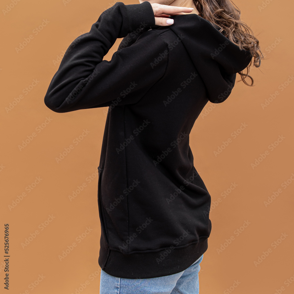 Black hoodie on woman. Long warm sleeve and patch pocket. Clothing for autumn or winter. Brown background. Square Black hoodie on woman. Long warm sleeve and patch pocket. Clothing for autumn or winter. Brown background. Square