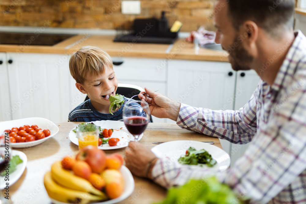 Happy father feeding his small boy while having lunch in the kitchen Happy father feeding his small boy while having lunch in the kitchen