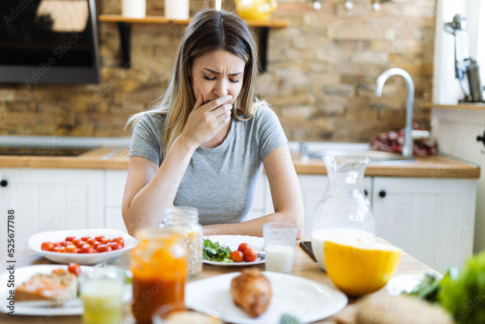 Young woman feeling nausea during breakfast time at dining table