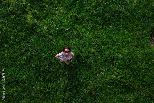Portrait of happy cute young woman with short hair in casual black and white striped shirt, red round eyeglasses lying down on green grass and looking at camera through glasses.outdoor summertime shot