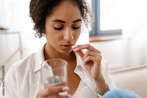 Young black woman being upset and taking abortion pill at home photo