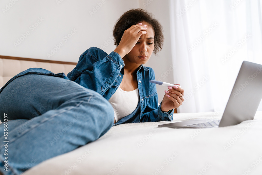 Young woman holding pregnancy test and using laptop in bed at home Young woman holding pregnancy test and using laptop in bed at home