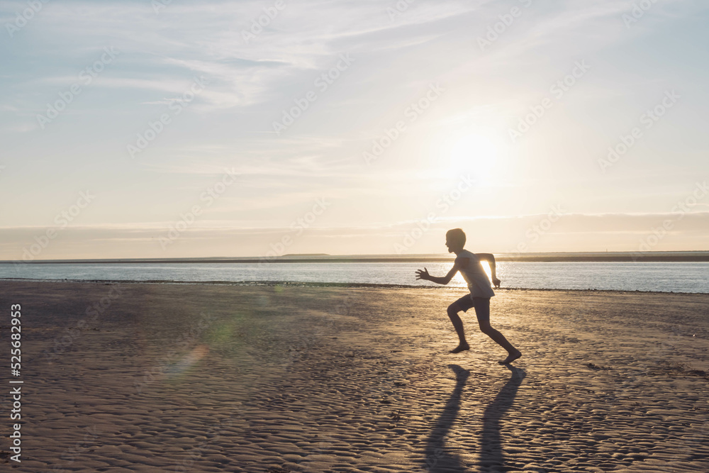 a silhouette of a child running on the beach on the sand near the water, at sunset there is a place for an inscription