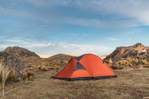 orange colored camp in the mountains in a sunset surrounded by rocks and yellow vegetation in the winter in the andes mountain range © roy