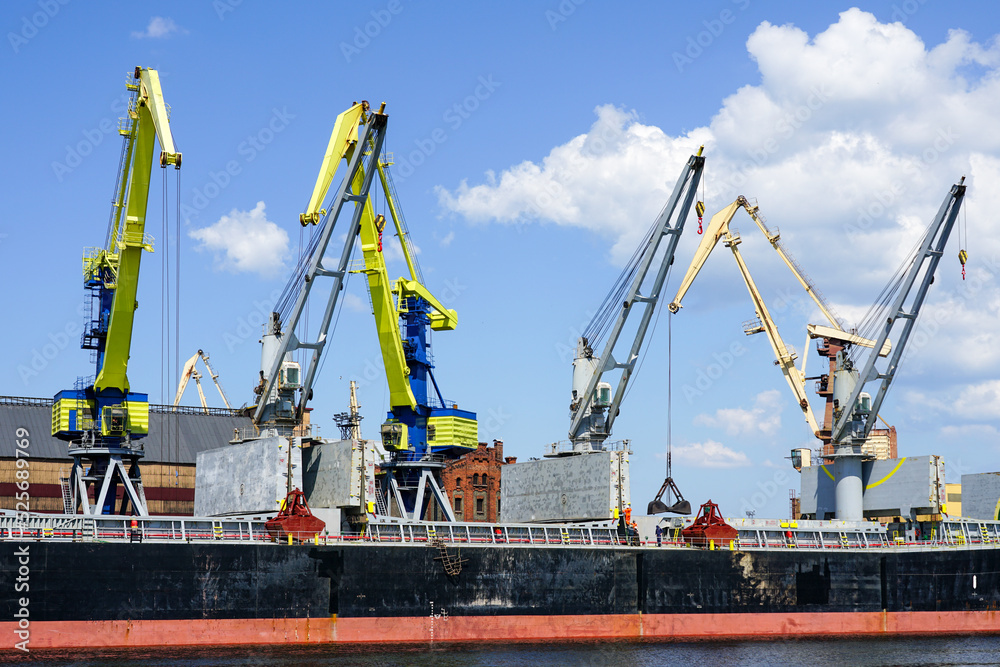 Bulk carrier with open storage tanks in port bulk terminal, port cranes with buckets ready for work