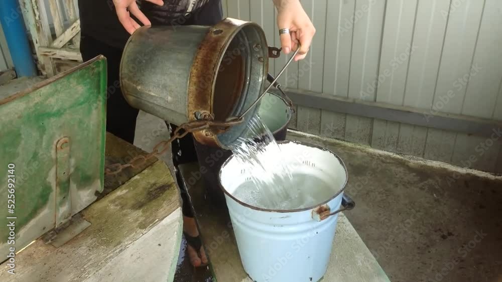 Gardener pours water from well into buckets against fence Gardener pours water from well into buckets against fence