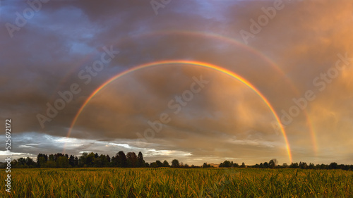Double rainbow over the field after rain at colorful dramatic sunset