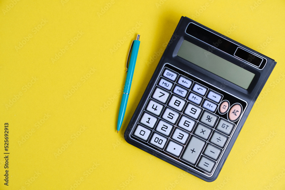 Calculator turned off and a ballpoint pen on yellow background. Calculator turned off and a ballpoint pen on yellow background.