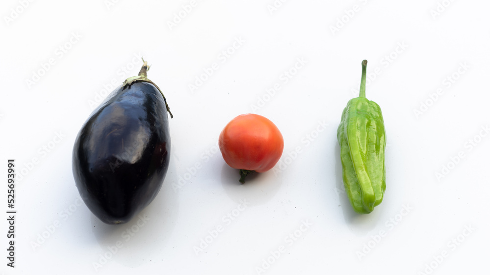 group of an organic eggplant, tomato and pepper from the garden on a white surface group of an organic eggplant, tomato and pepper from the garden on a white surface