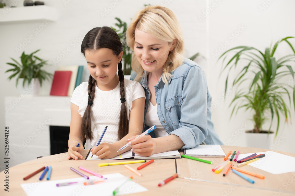 Obraz premium Mother and daughter beautiful and happy make a card for mother's day sitting together at the table with paper and pencils